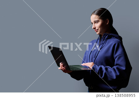 Portrait of smiling teenage girl holding laptop on gray studio background 138508955