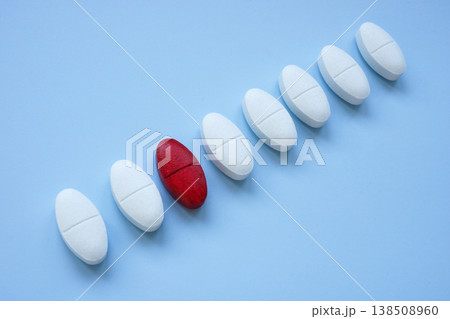 Red pill among white tablets depicting uniqueness. 138508960