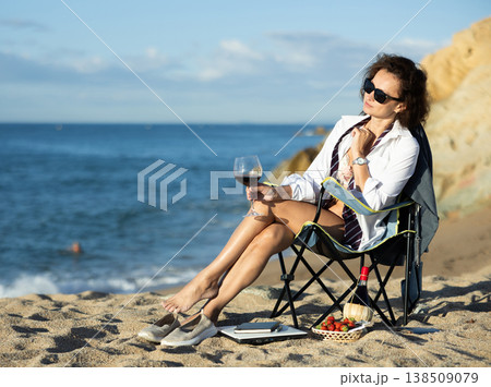 Naked businesswoman in shirt relaxing on sea beach with glass of red wine and picnic basket 138509079
