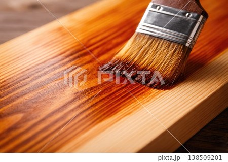 Applying wood stain with brush on natural wooden surface close up 138509201