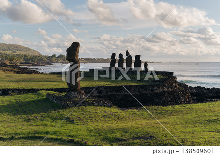 Majestic moai stone statue stands on green grassy coast of rapa nui easter island under bright cloudy sky offering serene mysterious expression overlooking vast blue ocean 138509601