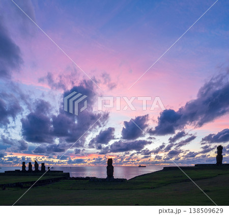 Majestic moai monument stands on easter island rapa nui grass field under deeply peaceful sunset sky filled with purple cloud reflecting ancient mystery across dark ocean horizon Majestic moai monument stands on easter island rapa nui grass field under deeply peaceful sunset sky filled with purple cloud reflecting ancient mystery across dark ocean horizon 138509629