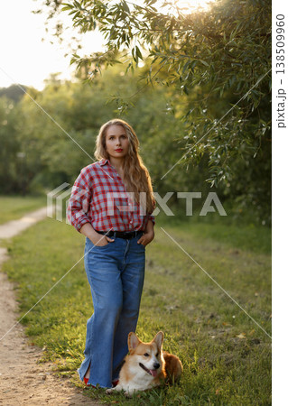 Young Woman Smiling. Relaxed Young Woman In Plaid Shirt With Dog On Sunlit Park Pathway 138509960
