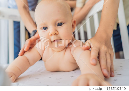 Baby lying on stomach in crib with parents hands gently placed on back showing protection and care. Safe newborn surrounded by love and support. Family security, parenting and trust concept 138510540