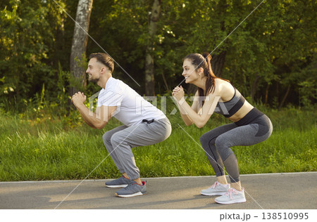 Sporty couple doing squat in green outdoor park, fit man and woman squatting, exercising together Sporty couple doing squat in green outdoor park, fit man and woman squatting, exercising together 138510995