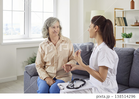 Portrait of sick senior woman sitting at on sofa at home with a young female nurse supporting her. Portrait of sick senior woman sitting at on sofa at home with a young female nurse supporting her. 138514296