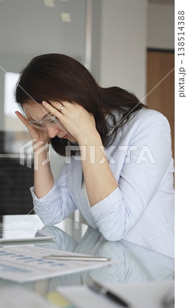 Businesswoman clutching her head in an office, exhausted and tense from a severe headache while surrounded by financial reports and paperwork, overwhelmed by pressure and burnout, vertical view Businesswoman clutching her head in an office, exhausted and tense from a severe headache while surrounded by financial reports and paperwork, overwhelmed by pressure and burnout, vertical view 138514388