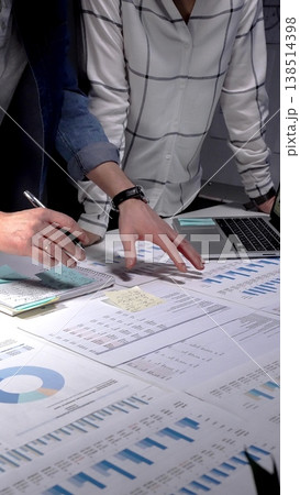 Collaboration of business professionals analyzing financial charts and data on papers and tablet, working late on a new strategy for company success Collaboration of business professionals analyzing financial charts and data on papers and tablet, working late on a new strategy for company success 138514398