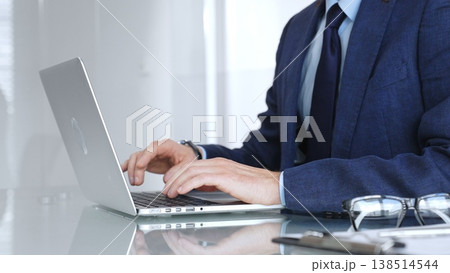 Professional businessman working on laptop computer, typing on keyboard in modern office, managing business tasks. Business people concept 138514544