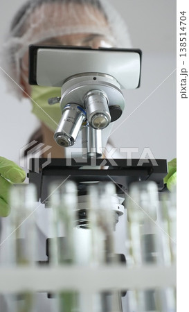 Close up of scientific precision involving green gloved hands adjusting microscope lens, blurred laboratory glassware highlighting medical investigation. Medicine, laboratory and science concept Close up of scientific precision involving green gloved hands adjusting microscope lens, blurred laboratory glassware highlighting medical investigation. Medicine, laboratory and science concept 138514704