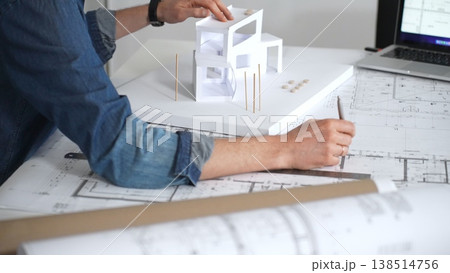 Architect hands reviewing building blueprints and housing plans on a table, utilizing a laptop for architectural drawing and design while planning a construction project 138514756