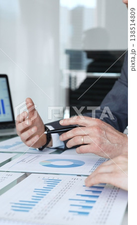 Businessman's hands analyzing financial data and charts on documents during a meeting, focusing on strategic planning and corporate growth in an office setting 138514809
