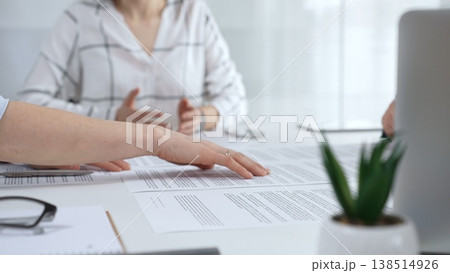 Business people discussing contract documents on a white desk, analyzing clauses and terms during an office meeting, collaborating on important paperwork for agreement Business people discussing contract documents on a white desk, analyzing clauses and terms during an office meeting, collaborating on important paperwork for agreement 138514926