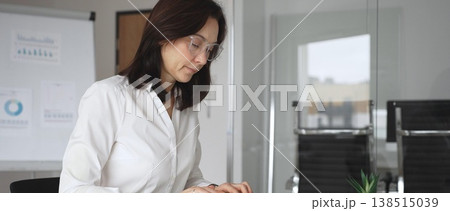 Businesswoman in white blouse and glasses sitting at a modern desk, working with a tablet in a contemporary office, focusing on digital tasks, using technology for efficient workflow Businesswoman in white blouse and glasses sitting at a modern desk, working with a tablet in a contemporary office, focusing on digital tasks, using technology for efficient workflow 138515039
