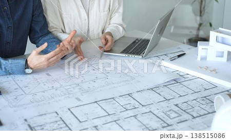 Engineering professionals collaborating on an architectural blueprint, using a compass to design a modern building, planning construction with a house model and laptop Engineering professionals collaborating on an architectural blueprint, using a compass to design a modern building, planning construction with a house model and laptop 138515086