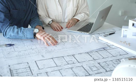 Two architects collaborate over blueprints and a model, using a compass and laptop to measure and plan detailed floor plans, symbolizing teamwork in property development Two architects collaborate over blueprints and a model, using a compass and laptop to measure and plan detailed floor plans, symbolizing teamwork in property development 138515110