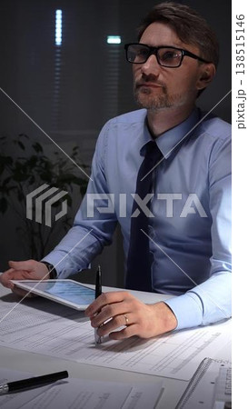 Businessman working late analyzing financial data at office, holding tablet with charts, writing notes on documents. Audit and taxes in business 138515146