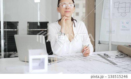 Professional architect woman working on architectural plans. Finding inspiration for a new building project. Smiling with satisfaction and confidence in her modern office Professional architect woman working on architectural plans. Finding inspiration for a new building project. Smiling with satisfaction and confidence in her modern office 138515246