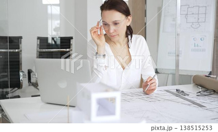 Female architect designing new blueprints for a project, reflecting on building plans and architectural models in a modern office environment, thinking about construction and innovation Female architect designing new blueprints for a project, reflecting on building plans and architectural models in a modern office environment, thinking about construction and innovation 138515253