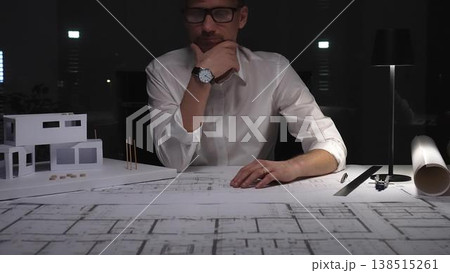 Architect working late on blueprints and house model, designing a new building project for construction. Business and architect people concept Architect working late on blueprints and house model, designing a new building project for construction. Business and architect people concept 138515261