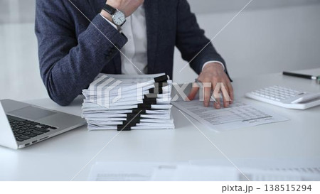 Business professional organizing documents at desk, managing paperwork and financial reports, working on taxes or corporate accounts with a laptop and calculator for audit preparation. Audit and taxes Business professional organizing documents at desk, managing paperwork and financial reports, working on taxes or corporate accounts with a laptop and calculator for audit preparation. Audit and taxes 138515294