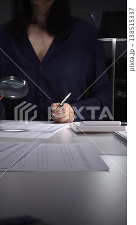 Woman examining tax forms and financial statements at desk, using calculator and magnifying glass to verify figures and audit records. Audit and taxes theme in business 138515337