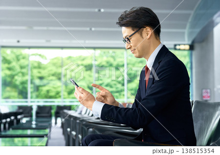 オフィスラウンジでスマートフォンを操作する笑顔の日本人男性ビジネスマン オフィスラウンジでスマートフォンを操作する笑顔の日本人男性ビジネスマン 138515354
