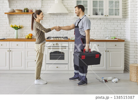 Repairman in uniform shaking hands with woman after successful repair standing in kitchen Repairman in uniform shaking hands with woman after successful repair standing in kitchen 138515387