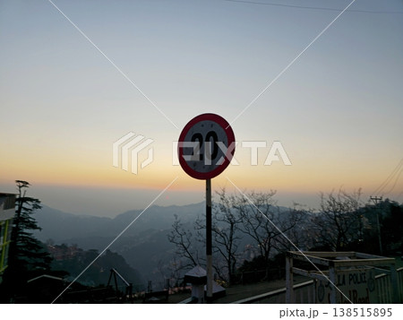 Roadside speed limit sign overlooking a valley in Shimla at sunset, with soft gradient sky and layered mountains, symbolizing slow travel and mountain roads. 138515895