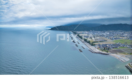 早春の富山県東部、小川の河口周辺からの眺め、雲に隠れている北アルプスや洋上風力発電風車たちの様子 138516613