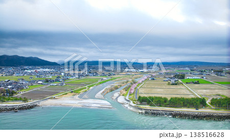 早春の富山県東部、小川の河口周辺からの眺め、雲に隠れている北アルプスや洋上風力発電風車たちの様子 138516628