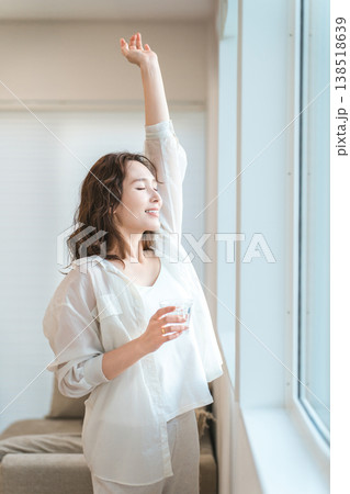 朝リビングの窓際で深呼吸しながら水分補給するアジア人女性 朝リビングの窓際で深呼吸しながら水分補給するアジア人女性 138518639