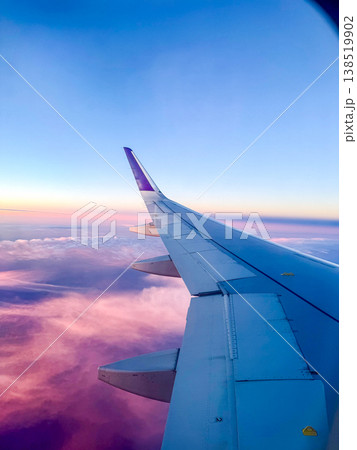 Airplane wing against a colorful sky at sunset. Soft clouds are visible below, creating a serene travel atmosphere. 138519902