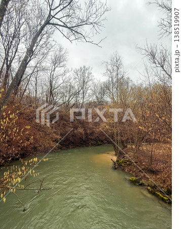 A serene river flows through a wooded area in Geislingen, Germany. The landscape features bare trees and autumn foliage along the banks. 138519907