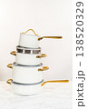 A vertical composition of four stacked ceramic pots in matte white finish, each with golden handles and matching lids. Photographed against a neutral background on a marble surface. Great for 138520329
