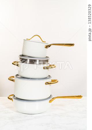 A vertical composition of four stacked ceramic pots in matte white finish, each with golden handles and matching lids. Photographed against a neutral background on a marble surface. Great for 138520329