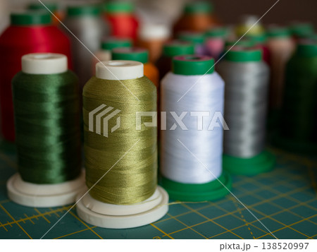 Colorful spools of sewing and embroidery thread arranged on a cutting mat. The vibrant threads showcase a variety of textures and hues for creative textile projects Colorful spools of sewing and embroidery thread arranged on a cutting mat. The vibrant threads showcase a variety of textures and hues for creative textile projects 138520997