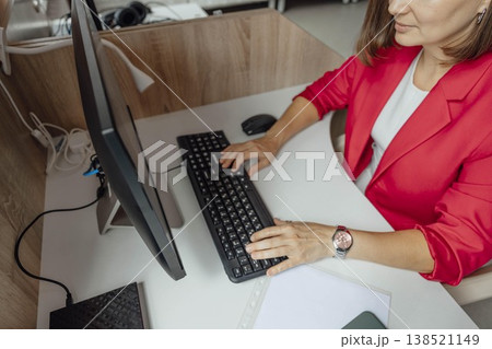 young Caucasian woman with brown hair works at a computer in a modern coworking office. The space features wooden furniture and a library in the background, top view 138521149