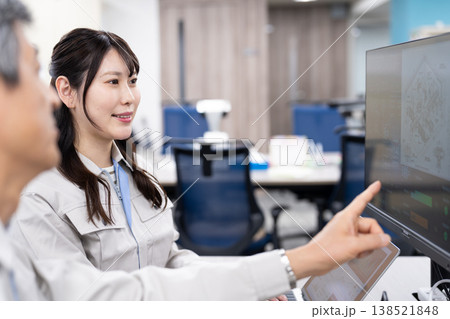 パソコンの画面を見ながら打ち合わせをする作業着の男女 パソコンの画面を見ながら打ち合わせをする作業着の男女 138521848