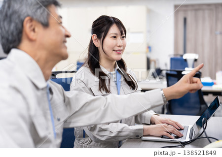 パソコンの画面を見ながら打ち合わせをする作業着の男女 パソコンの画面を見ながら打ち合わせをする作業着の男女 138521849