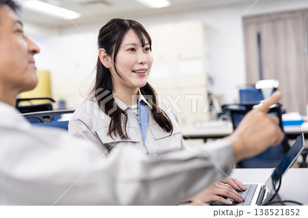 パソコンの画面を見ながら打ち合わせをする作業着の男女 パソコンの画面を見ながら打ち合わせをする作業着の男女 138521852