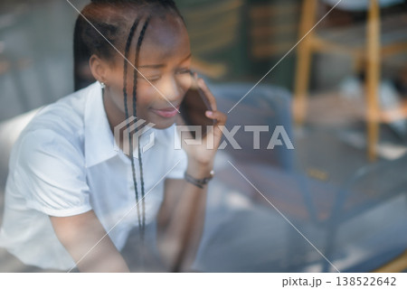 Young Black woman speaking on smartphone behind cafe window, seen through glass reflections. Candid business lifestyle, remote conversation, modern communication and indoor connection. Young Black woman speaking on smartphone behind cafe window, seen through glass reflections. Candid business lifestyle, remote conversation, modern communication and indoor connection. 138522642