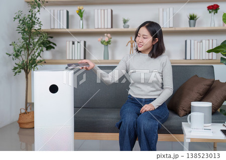 Woman using a remote to operate an air purifier Woman using a remote to operate an air purifier 138523013