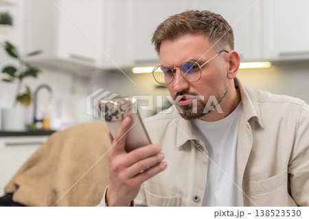 Young man with glasses checks smartphone reads tiny text surprised by news vision aid improves focus 138523530