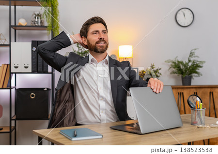 Middle-aged businessman finishes final report powers down laptop closes lid stretches smiles relaxed 138523538