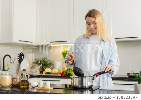 Young woman slowly seasoning homemade soup in pot on electric cooktop for healthy lunch at home 138523547