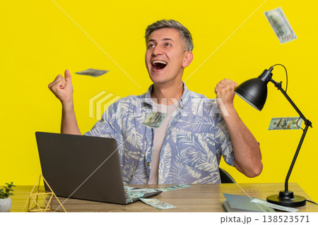 Adult man celebrating jackpot lottery win at laptop, falling cash money happy excited smiling face 138523571
