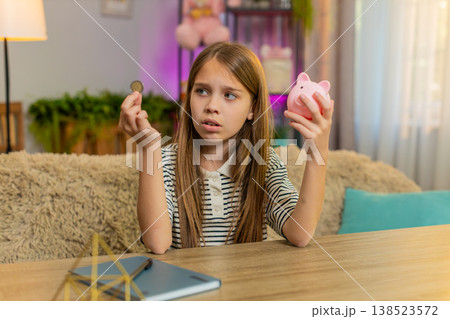 Child girl kid sadly looks at empty piggy bank shaking head at home table feeling disappointment Child girl kid sadly looks at empty piggy bank shaking head at home table feeling disappointment 138523572