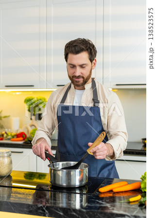 Middle-aged man seasoning homemade healthy soup on electric stove in home kitchen for hot diet meal Middle-aged man seasoning homemade healthy soup on electric stove in home kitchen for hot diet meal 138523575