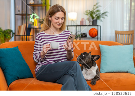 Middle-aged woman with dog enjoys morning coffee and reads news on smartphone relaxed mood indoors Middle-aged woman with dog enjoys morning coffee and reads news on smartphone relaxed mood indoors 138523615